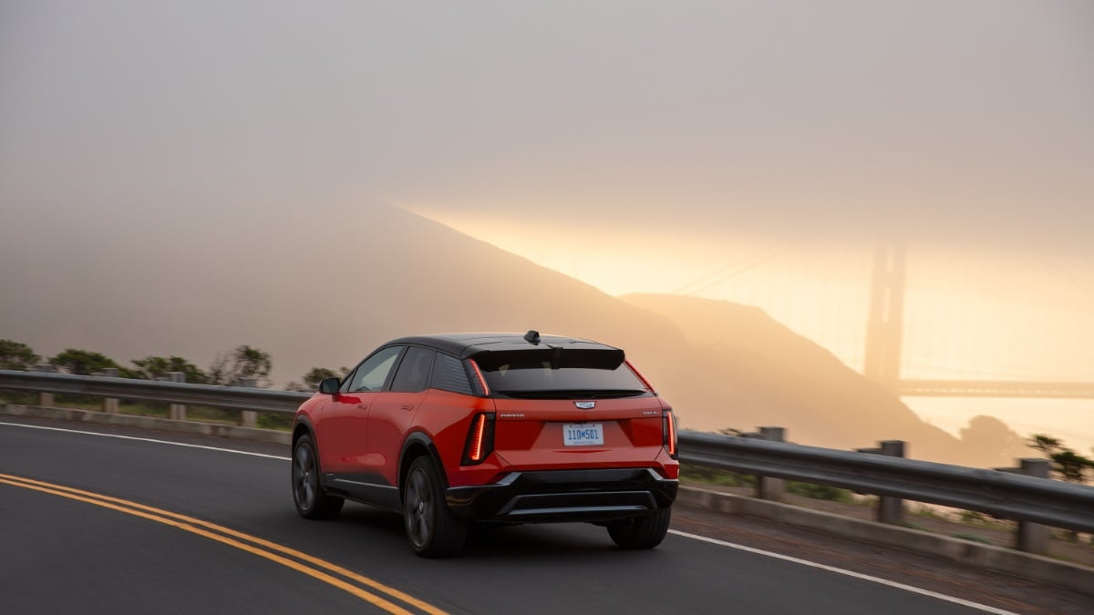 Red SUV driving on a coastal road with foggy Golden Gate Bridge in the background.