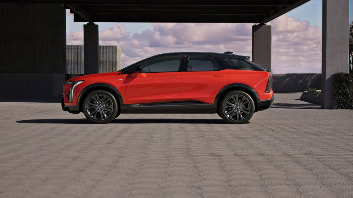 Red SUV parked under a modern structure with a cloudy sky in the background.
