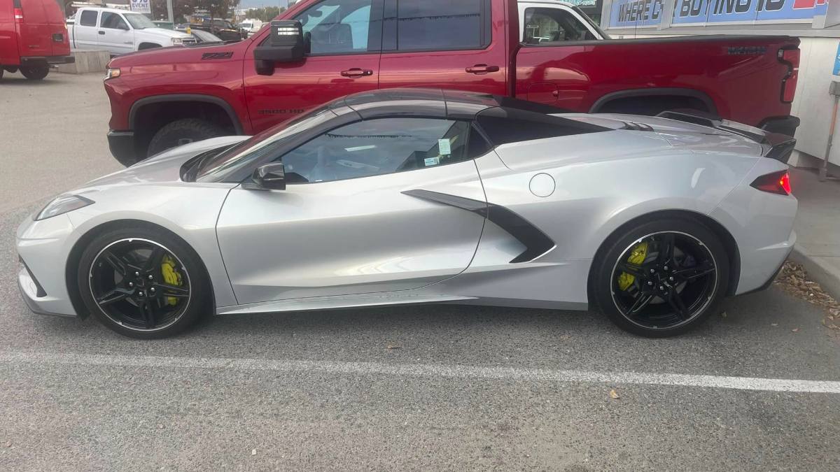 Silver 2023 Chevrolet Corvette C8 parked in lot, side profile view, featuring black wheels, yellow brake calipers, and aggressive aerodynamic styling.