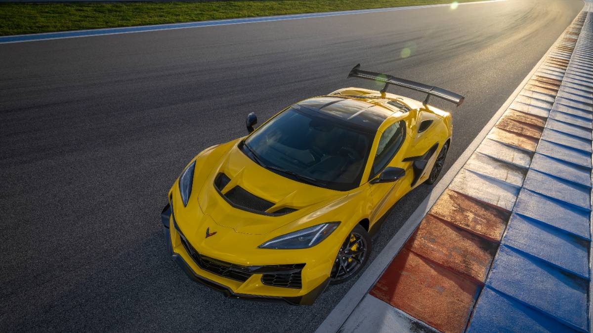Bright yellow Corvette Z06 with massive rear wing, parked on racetrack with curbing, showcasing aggressive sports car design