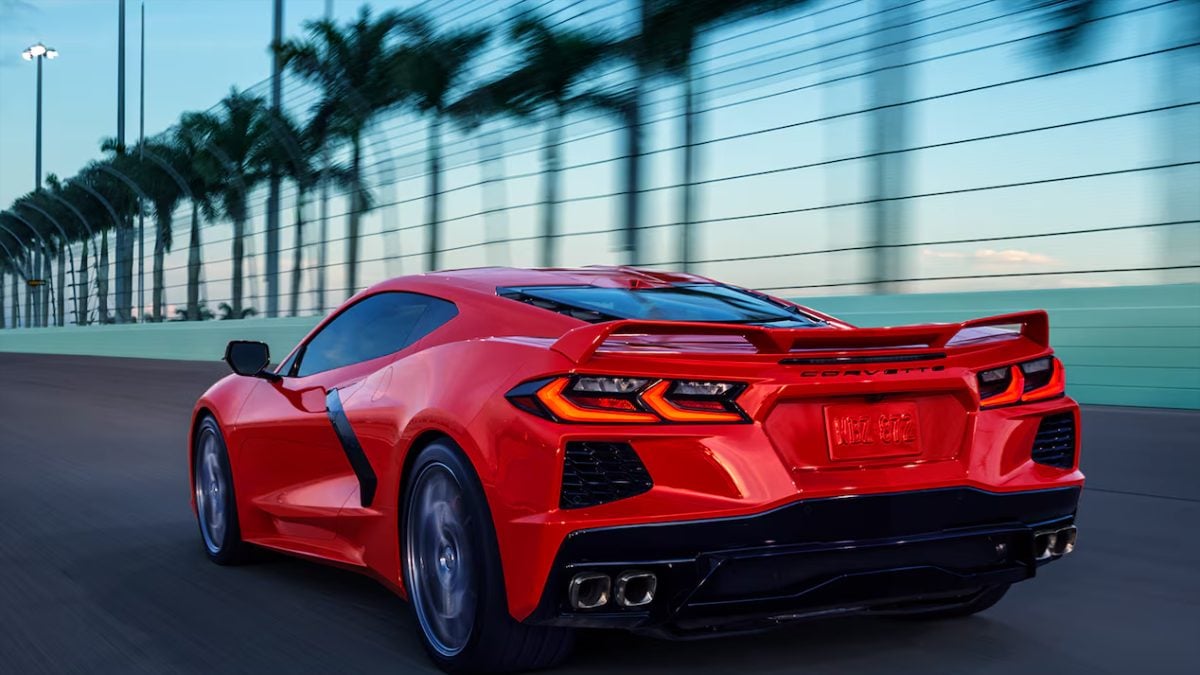 Bright red 2025 Corvette Z06 racing past palm trees with dynamic rear three-quarter view and aerodynamic lines