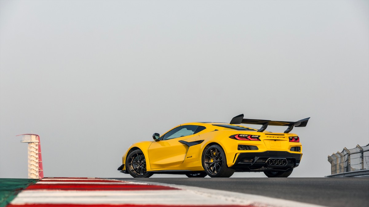 Bright yellow Chevrolet Corvette Z06 with massive rear wing on racing circuit, viewed from rear three-quarter angle