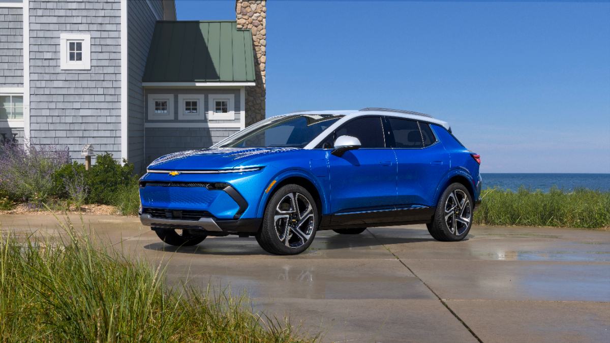 Bright blue Chevrolet Equinox EV parked on coastal concrete driveway with beach house and ocean backdrop