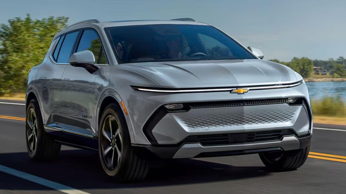 Silver 2025 Chevrolet Equinox EV crossover SUV driving on coastal highway with water and trees in background