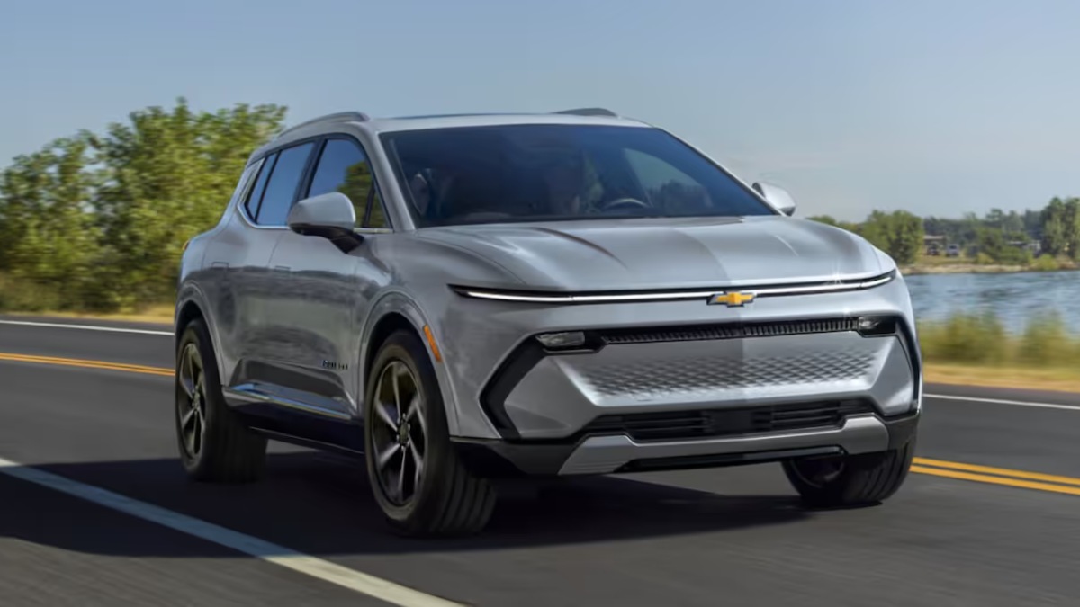 2025 Chevrolet Equinox EV in silver driving on a road near water, showcasing its sleek electric SUV styling, slim LED light bar, and modern front fascia.