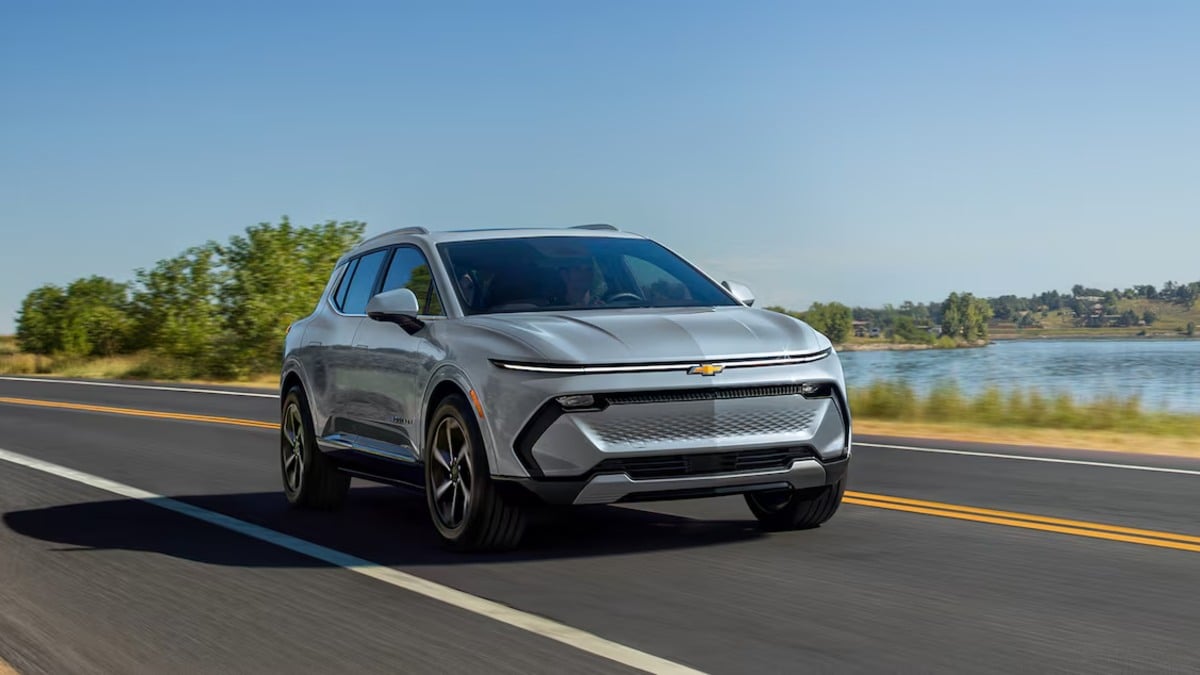 2025 Chevrolet Equinox EV in gray driving on a scenic road, showcasing updated front fascia, LED lighting, and compact electric SUV proportions.