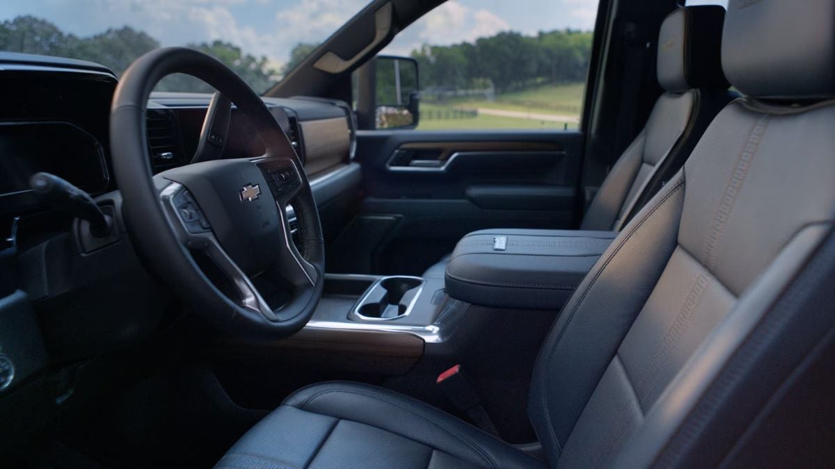 Interior of a Chevy Silverado featuring a steering wheel with Chevrolet emblem, black leather seats, and countryside view through the window, conveying comfort.