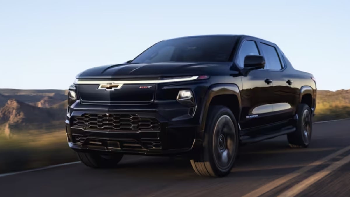 Black Chevrolet Silverado RST pickup truck, front three-quarter view, driving on highway with LED headlights and distinctive grille in desert landscape.