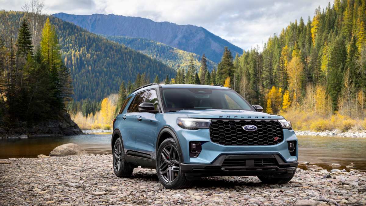 Light blue Ford Explorer ST parked on rocky riverbank with autumn mountain landscape behind