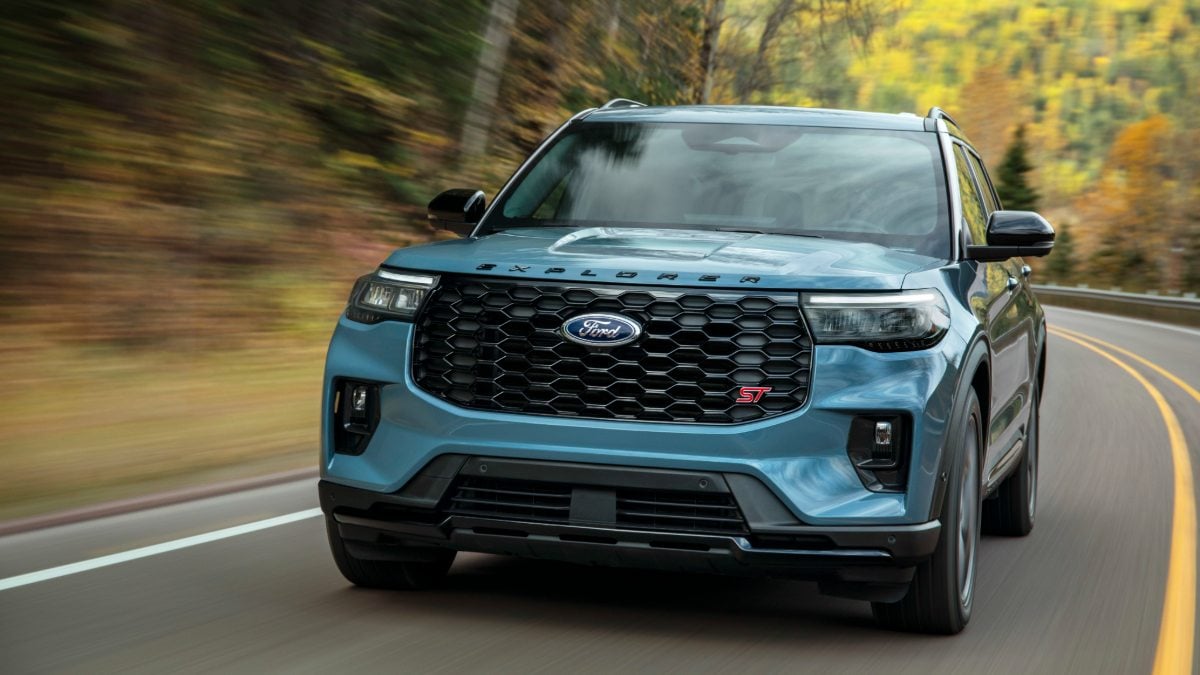 Light blue Ford Explorer ST driving on curved road through autumn forest