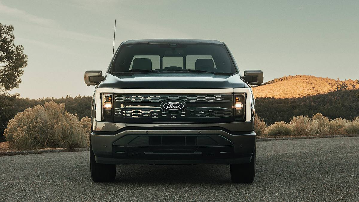 Front view of a Ford F-150 Lightning electric pickup parked on a mountain road with rugged landscape behind.
