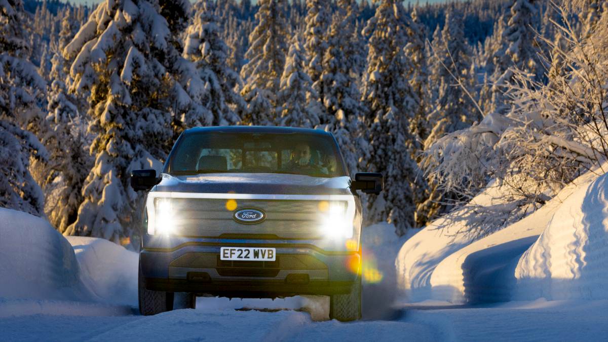 A Ford truck driving through a snowy forest, headlights on, showcasing its ability to navigate winter terrain.
