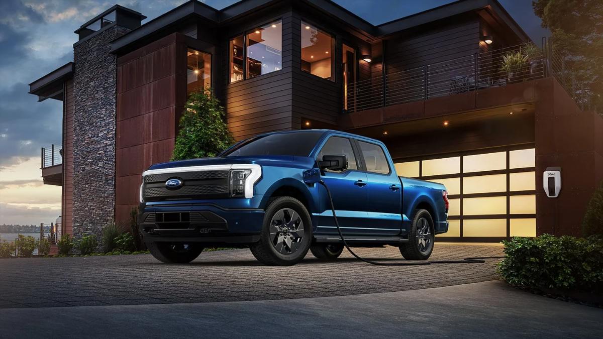 Blue 2025 Ford F-150 Lightning electric truck charging at modern home, sleek design with dark wheels and sunset sky