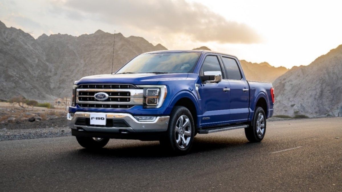 2025 Ford F-150 in metallic blue, front three-quarter view, showcasing chrome grille and LED headlights against mountainous desert backdrop at sunset.