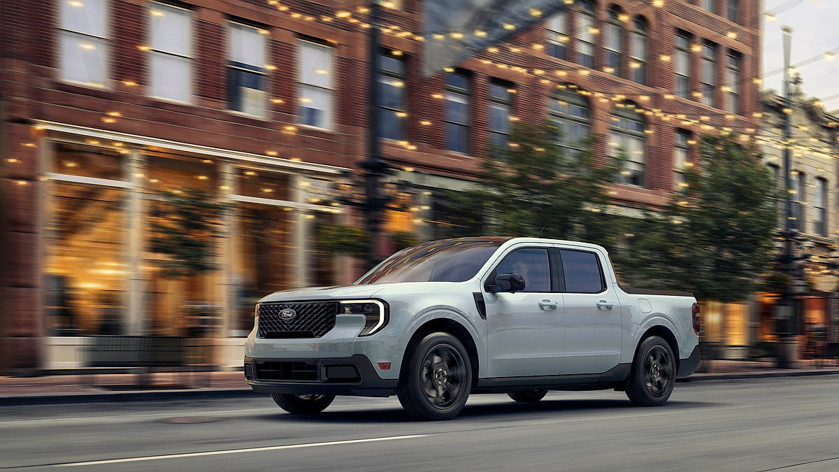 2025 Ford Maverick compact pickup driving through a city street at dusk, front three-quarter view