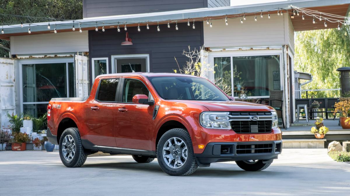 Red pickup truck parked in front of a modern house with large windows and string lights.