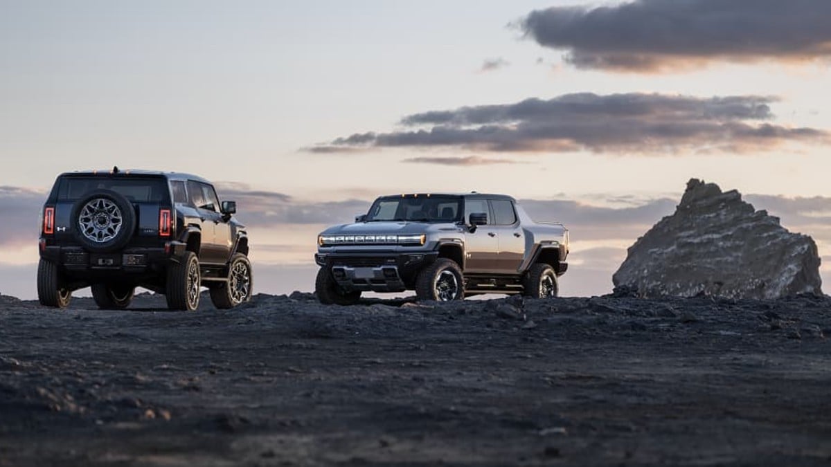 A 2025 GMC Hummer EV SUV shown from the front three-quarter view alongside its rear profile, displaying its massive grille and bold angular design in a studio setting.