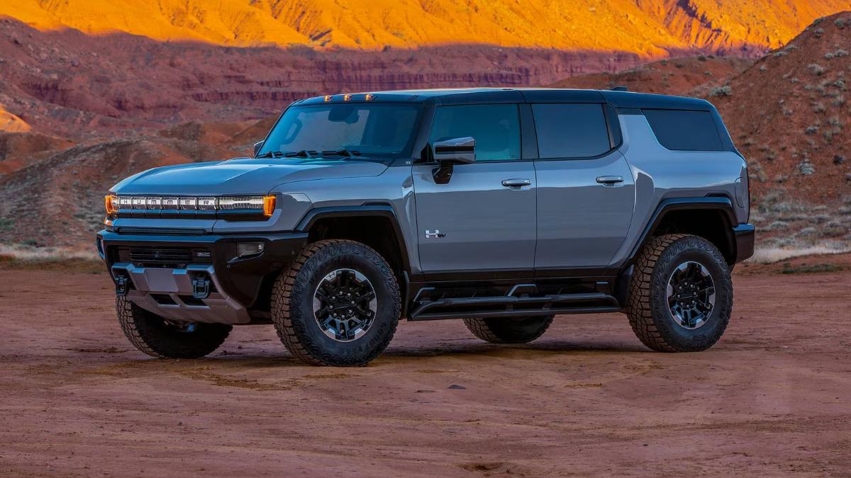 GMC Hummer EV SUV parked on red desert terrain with orange mountains at sunset