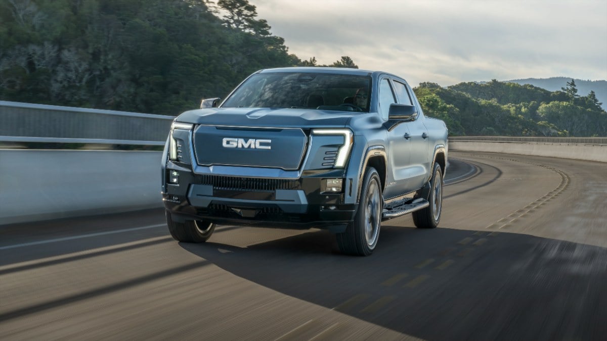 2025 GMC Sierra EV in blue, driving on a curved mountain road with forested landscape and misty sky