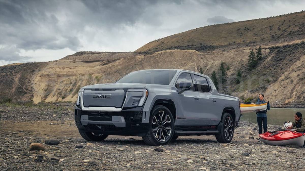 Silver 2025 GMC Sierra EV pickup truck parked on rocky terrain with kayaks, rugged mountain landscape in background