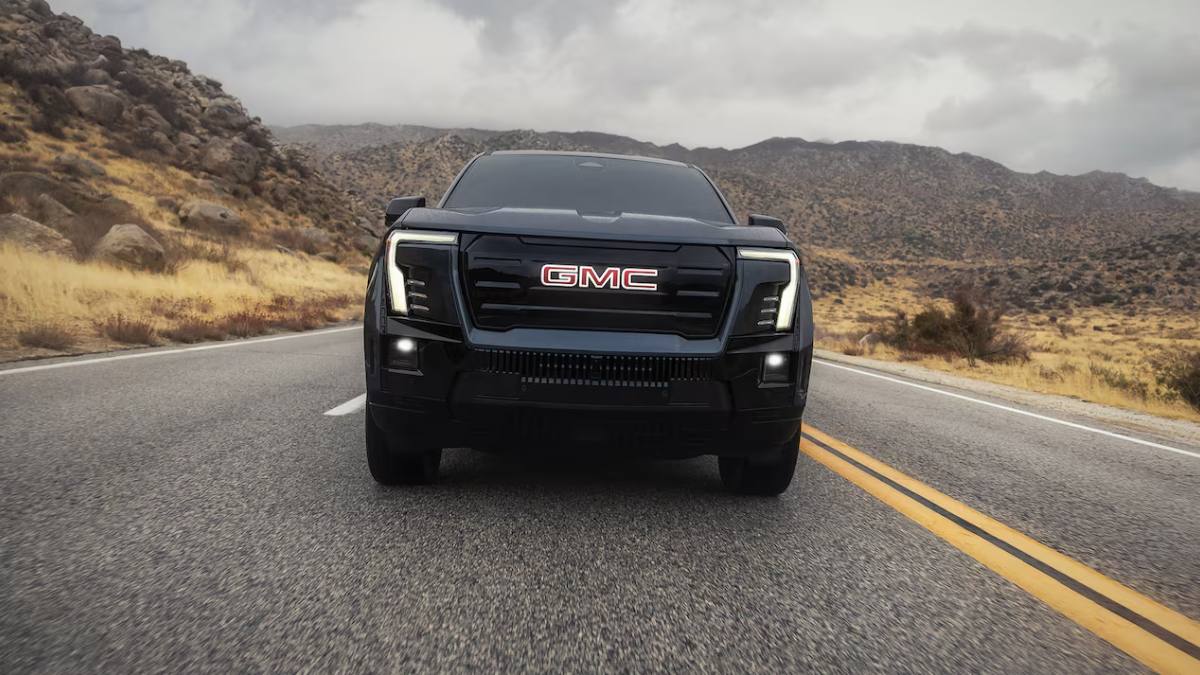 Black GMC pickup truck, front view on desert highway, featuring LED headlights and bold grille against mountainous landscape backdrop.