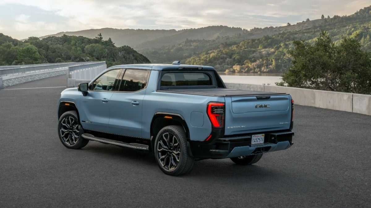A light blue 2024 GMC Sierra EV Denali Edition 1 pickup truck shown from the rear three-quarter view, parked on a mountain overlook with scenic hills in the background at dusk.