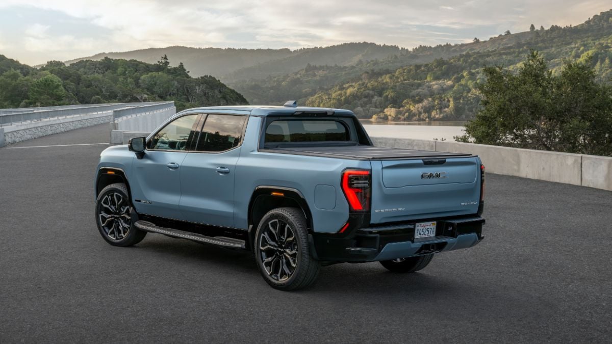 Blue pickup truck parked on a scenic road with hills and trees in the background.