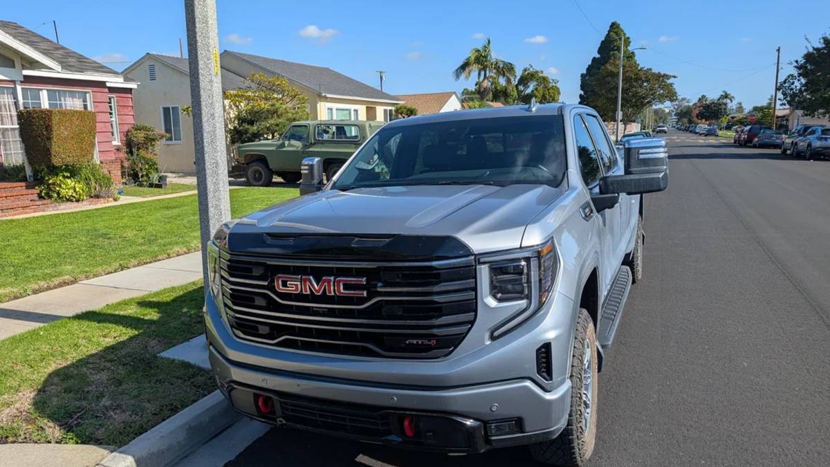 2025 GMC Sierra AT4 in gray parked on a suburban street, showing its bold grille, LED headlights, off-road tires, and rugged styling.