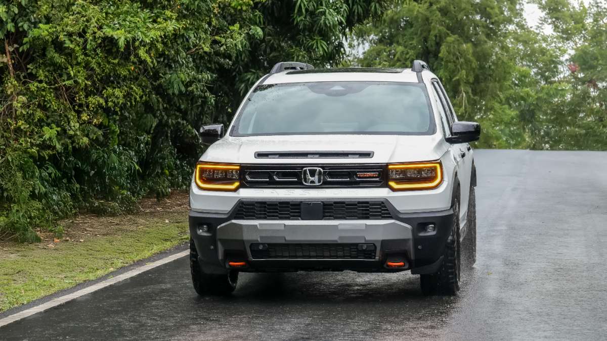 2024 Honda Passport in white, front three-quarter view, featuring distinctive LED headlights with amber accents, rugged black cladding, and off-road tires, parked on wet pavement surrounded by greenery.