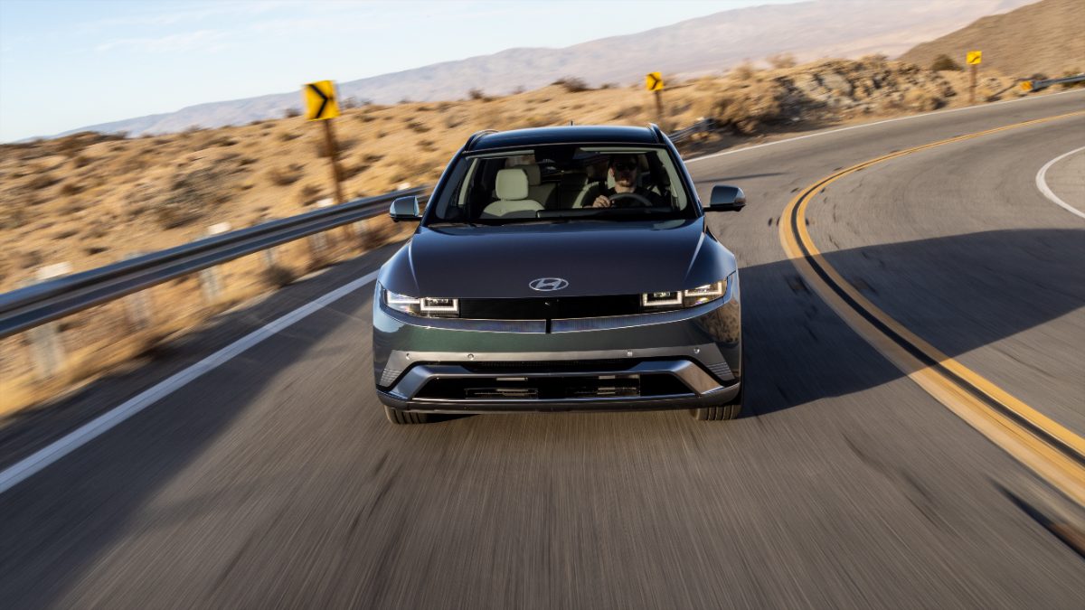 Dark blue Hyundai IONIQ 5 electric SUV driving on curved mountain road with yellow curve signs