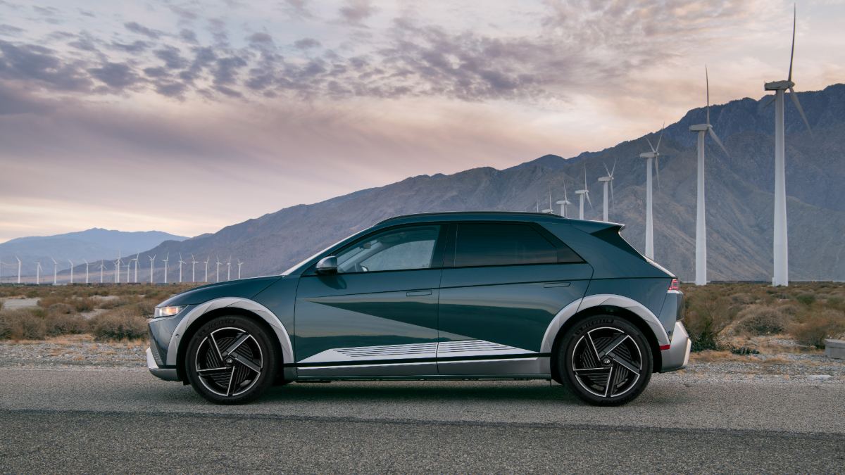 Electric car parked on a road with wind turbines and mountains in the background.