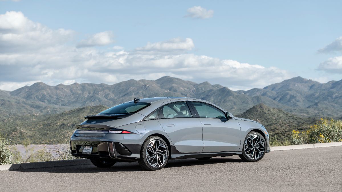 A silver sedan is parked on a road against a backdrop of lush, green mountains under a partly cloudy sky, conveying a sense of adventure.