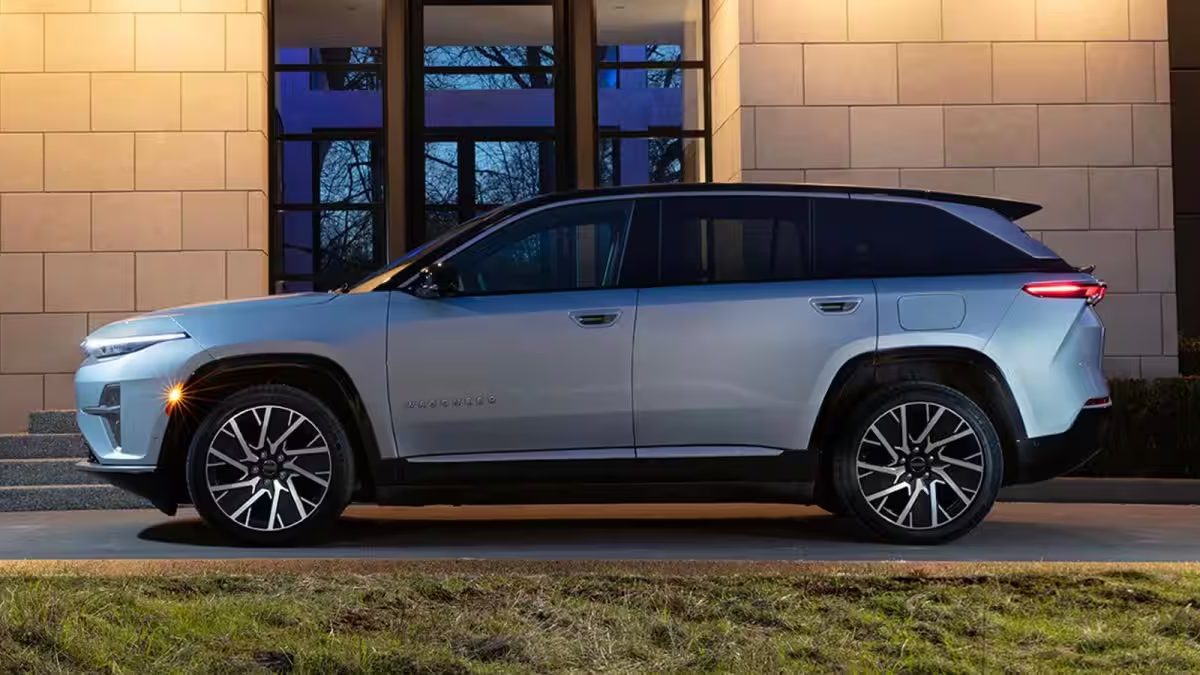 Silver Jeep Wagoneer SUV parked beside modern building at dusk, featuring distinctive black alloy wheels.