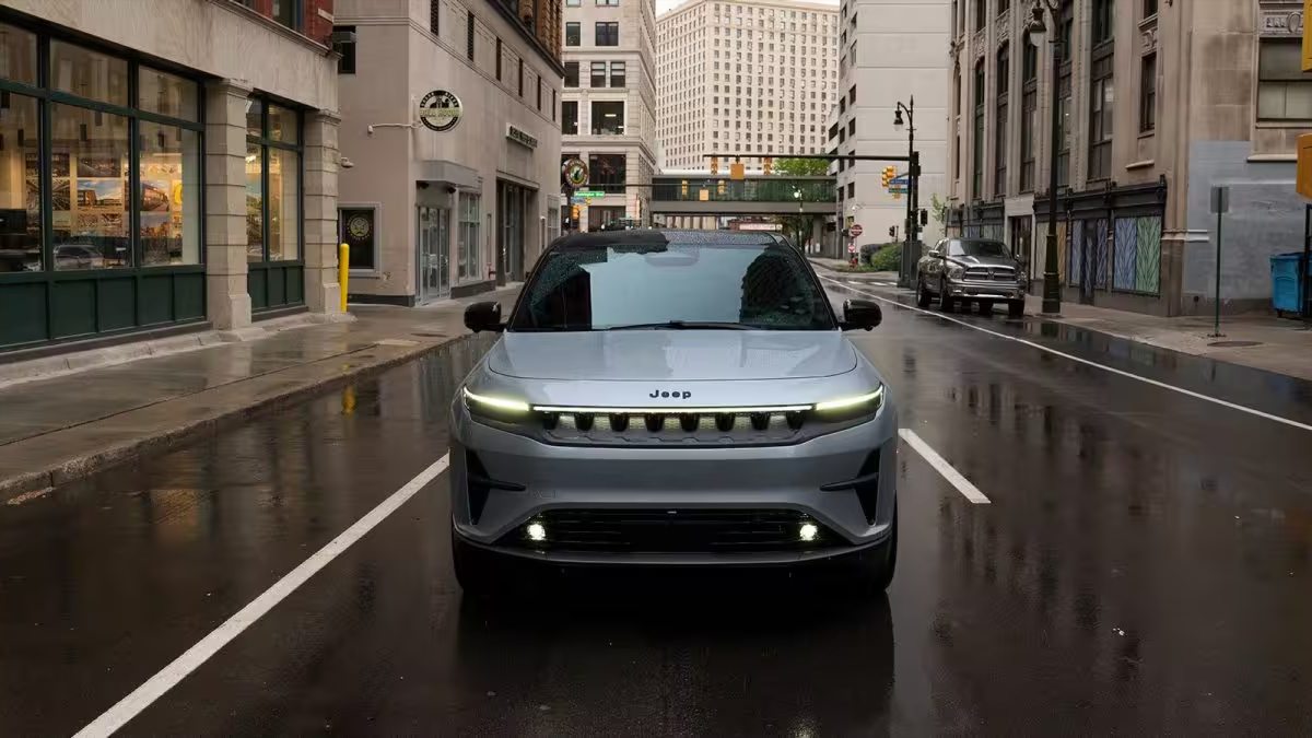 2025 Jeep Wagoneer electric SUV in silver, front-facing on wet urban street with modern buildings
