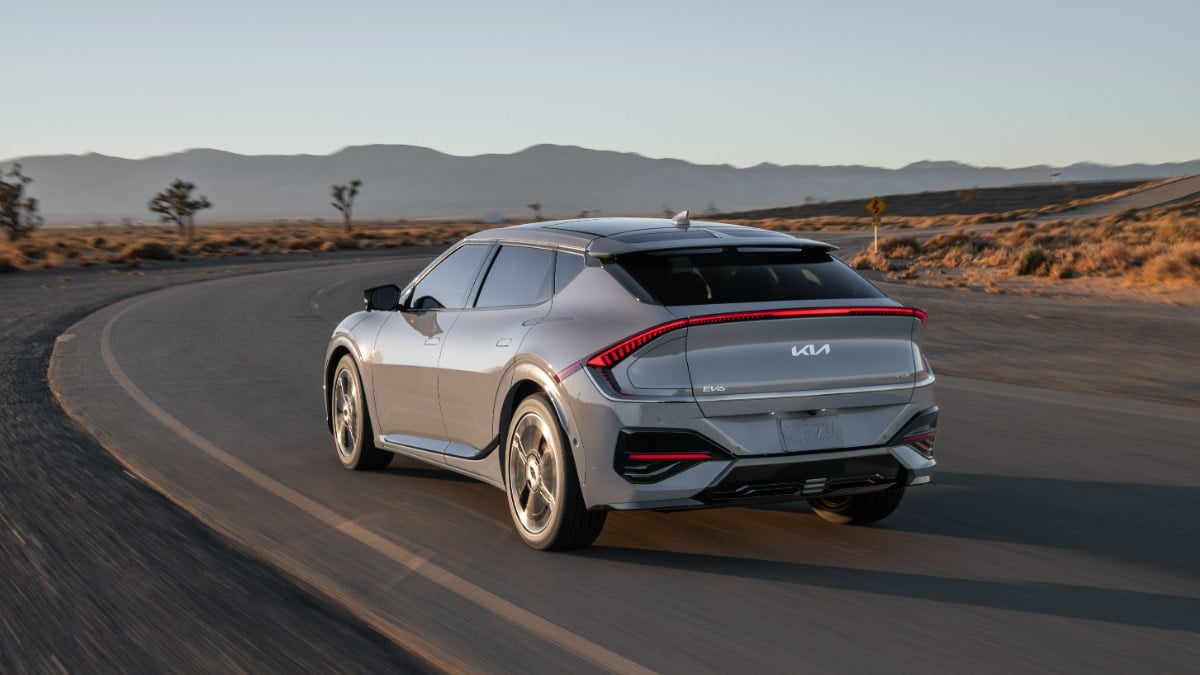 2024 Kia EV6 in silver, shown from rear three-quarter view on desert mountain road, featuring distinctive LED taillights and aerodynamic crossover design.