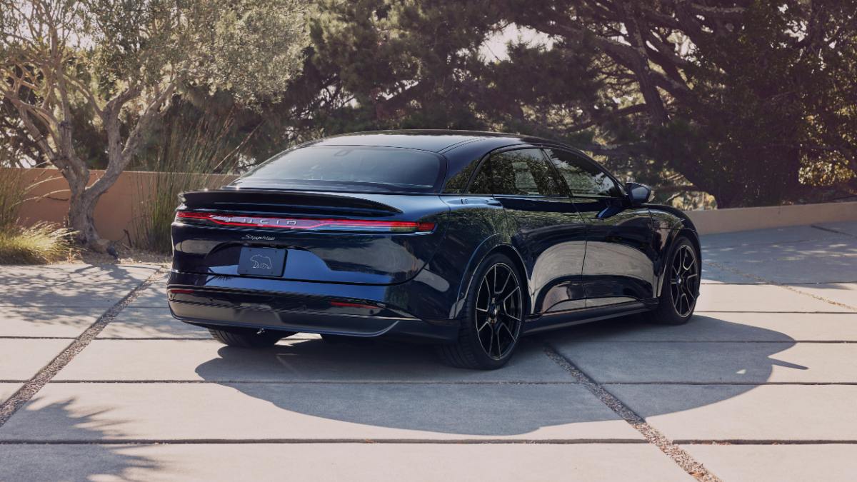 Dark blue Lucid Air luxury sedan parked on concrete driveway with landscaping behind