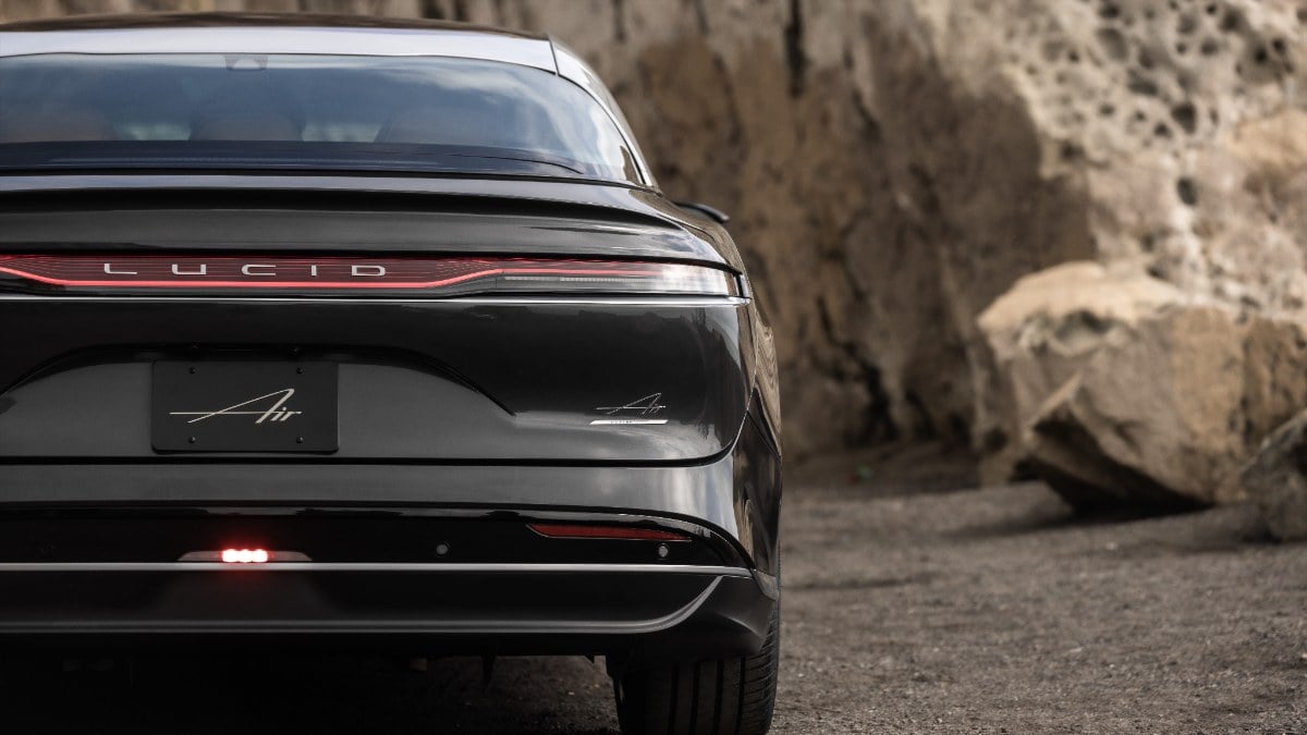 Black Lucid Air electric sedan rear view, illuminated red taillight, parked against rocky stone background
