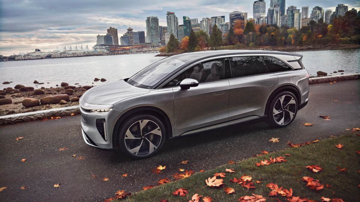 2026 Lucid Gravity in silver, side profile view, parked along Vancouver waterfront with fall foliage and downtown skyline backdrop.