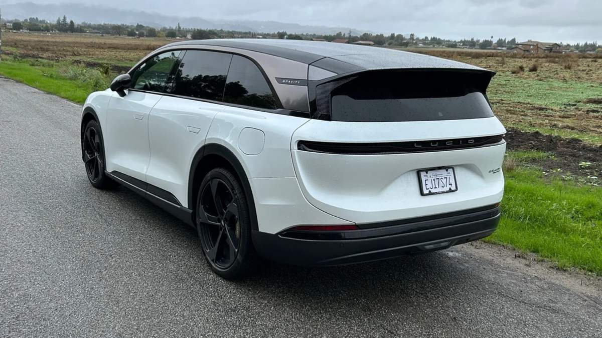 2025 Lucid Gravity electric SUV in pearl white, rear three-quarter view, featuring black glass roof and distinctive LED light bar, parked on rural road.