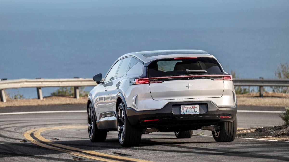 Silver Polestar electric SUV parked on coastal road, rear view with sleek LED taillights and curved design