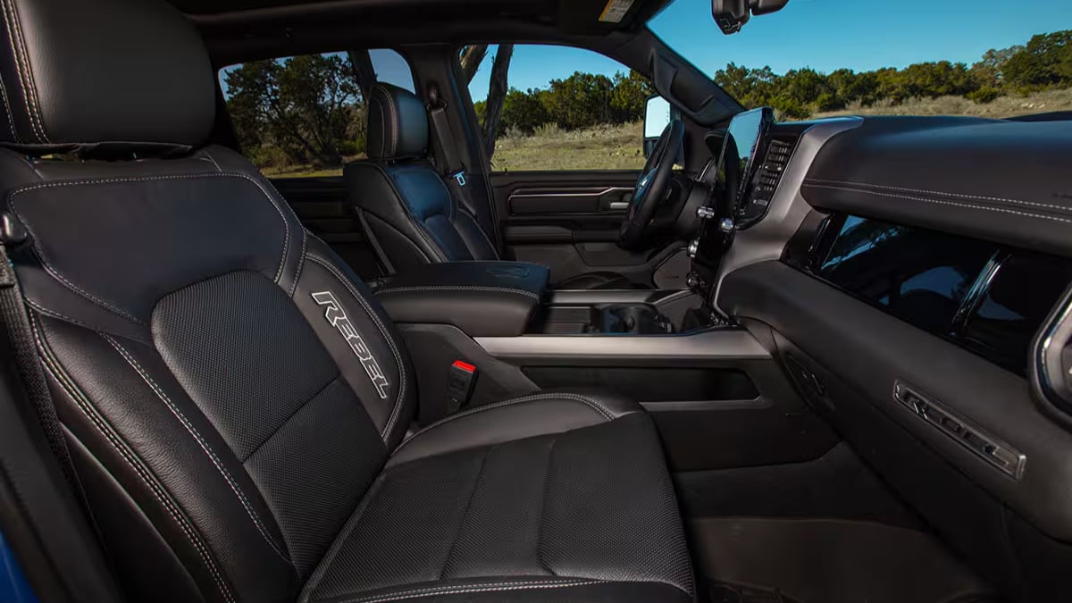 Interior of a 2025 Ram 1500 with black leather seats, a sleek dashboard, and a central touchscreen. The scene is well-lit, with greenery visible outside.