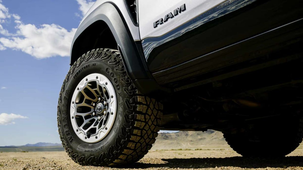 Close-up of a rugged off-road tire on a Ram 1500 RHO parked on a sandy desert landscape. The clear sky adds a sense of adventure and freedom.