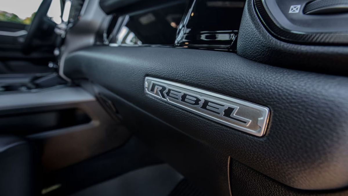 Close-up interior detail shot of a Ram Rebel badge on black leather dashboard trim, showing premium interior branding and materials.