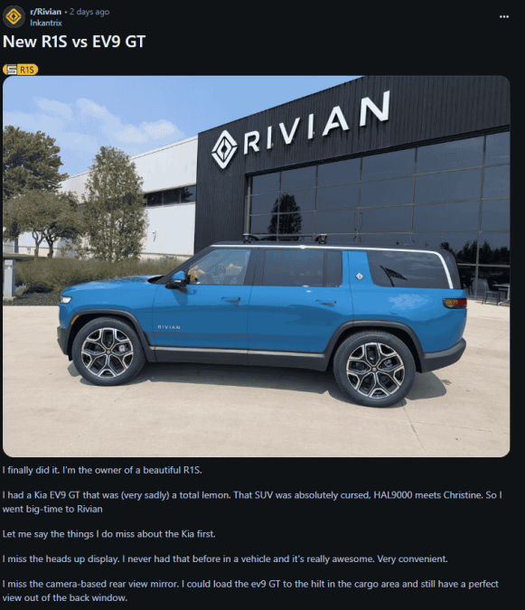 A blue Rivian R1S is parked outside a Rivian dealership, showcasing its sleek design and modern features against a backdrop of trees.