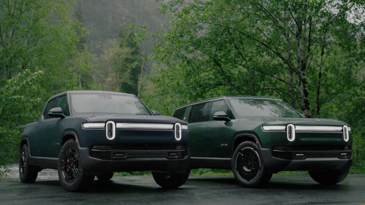 Two black Rivian R1S electric SUVs are shown from a front three-quarter angle, parked in a forested setting with distinctive vertical LED light bars across their front fascias.