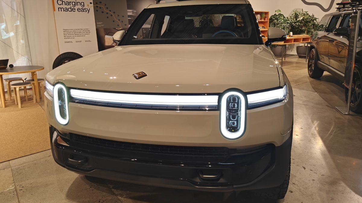 Rivian R1T electric SUV in champagne beige, close-up front quarter view showing distinctive Thor's Hammer LED headlight and wheel arch.