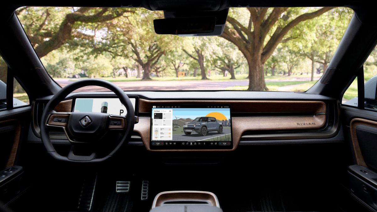 2025 Rivian R1T interior with wood-trimmed dashboard, digital screens, and tree-lined park view through windshield