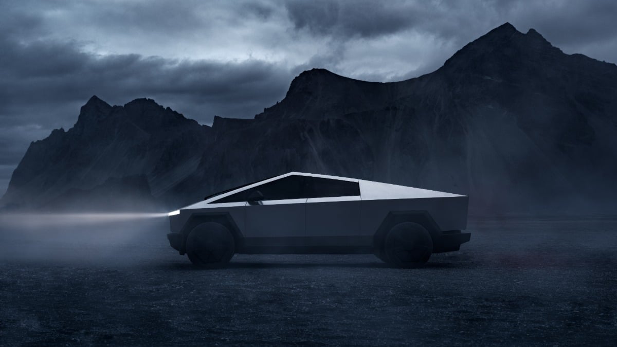 A silver Tesla Cybertruck shown in side profile against a dramatic mountainous backdrop with dark, moody storm clouds, highlighting its distinctive angular design and illuminated light bar.