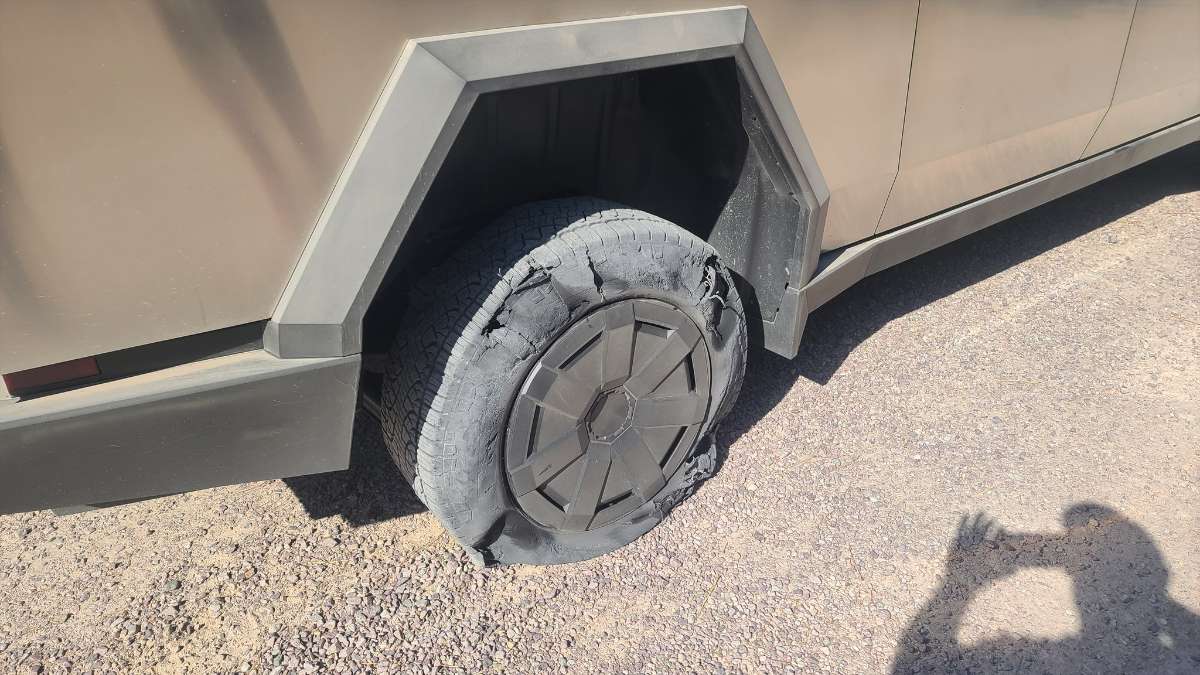 2025 Tesla Cybertruck wheel with angular fender, damaged tire on gravelly ground, geometric metallic design