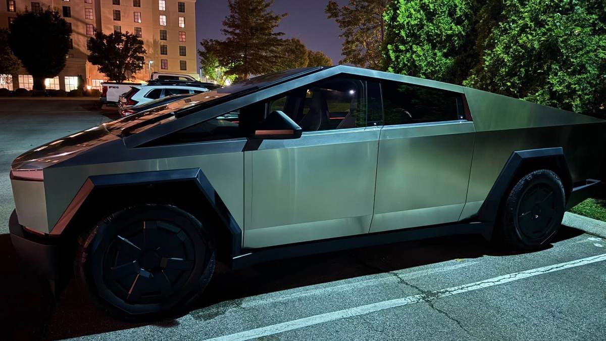 Tesla Cybertruck parked in nighttime lot, angular metallic body illuminated by street lights